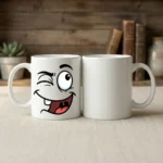 HL NOVA 11oz white ceramic coffee mug featuring a funny black cartoon winking face design, sitting on a desk with a rustic wooden background.