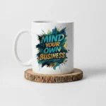 11oz White ceramic coffee mug with “Mind Your Own Business” text placed on a wooden stand.
