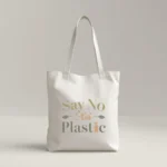 Durable eco-friendly white canvas tote bag with a minimalist typographic design in earth tones. The text 'Say No to Plastic' is printed in olive green and soft orange, accented with small leaf and seedling illustrations.