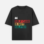 Front view of a premium black unisex oversized heavyweight t-shirt. The chest displays white quotation marks above the bold graphic statement "SELF CARE IS NOT SELFISH", with "SELF CARE" on a red background block, "IS NOT" on a yellow block, and "SELFISH" on a teal block. Features a loose crew neckline and relaxed slouchy sleeves.